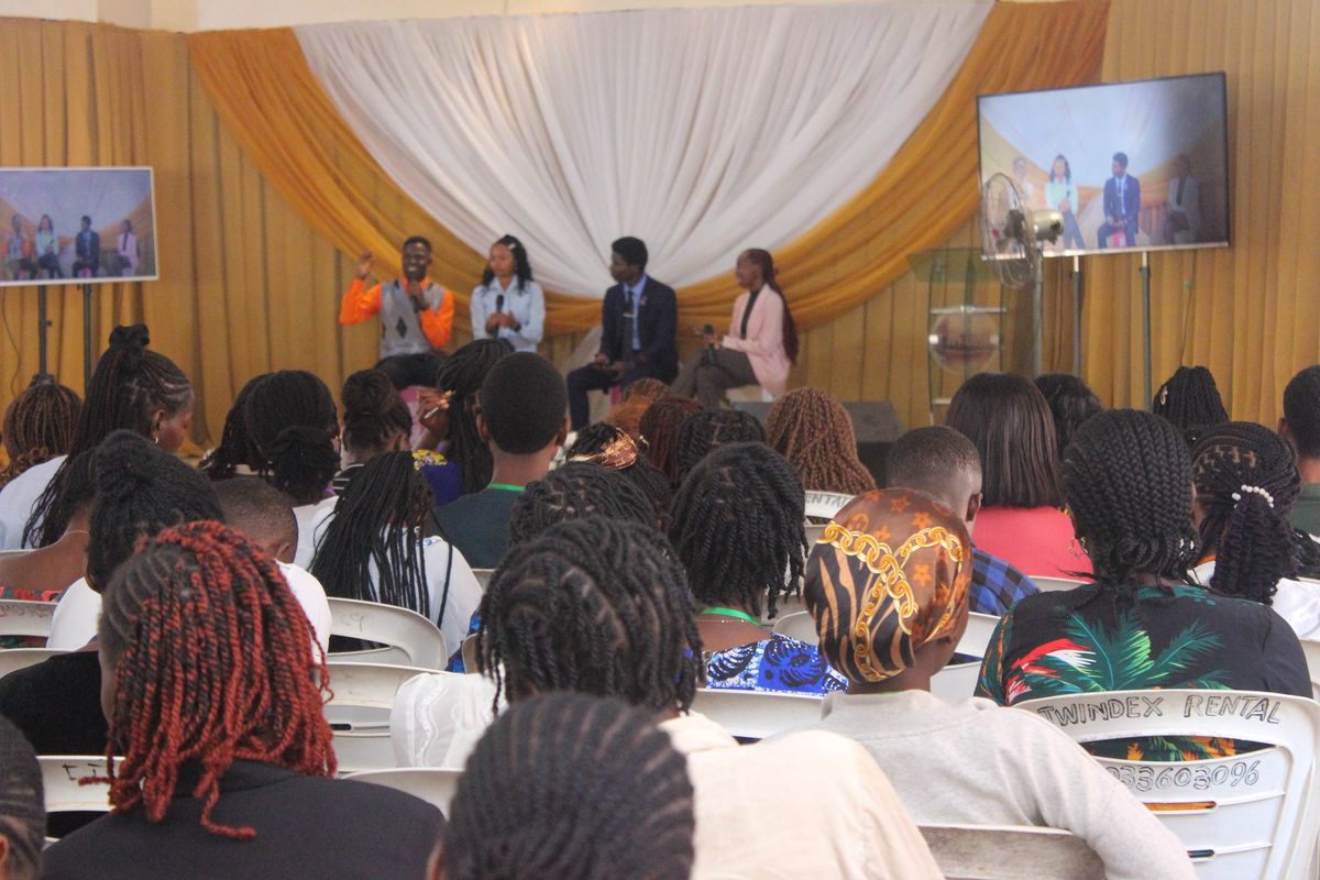 A panel of four speakers on stage leading a discussion, with the audience seated in front